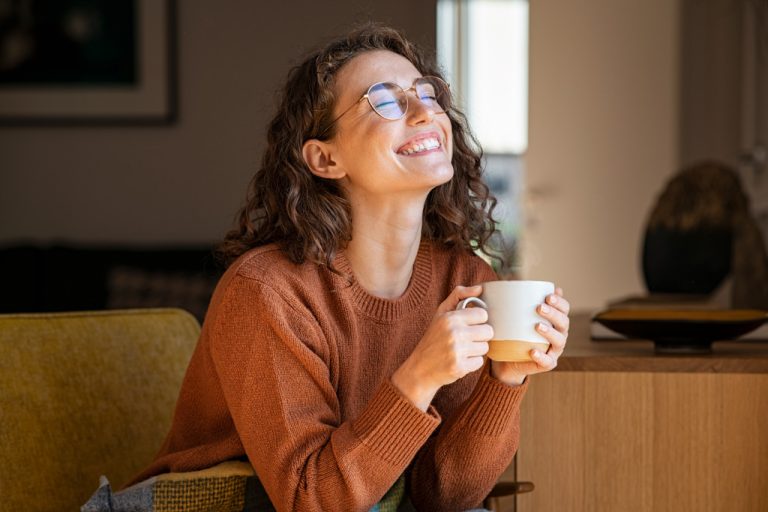 Young woman smiling while drinking tea and sitting on a couch at home.